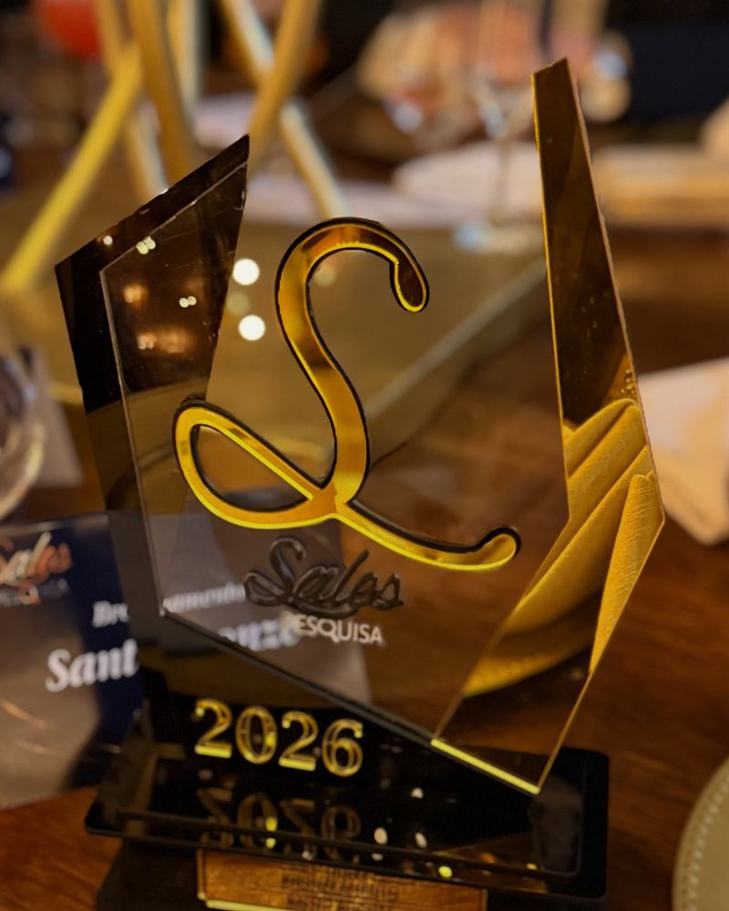 Troféu dourado do Sales Pesquisa 2026 entregue ao Santo Bronze, sobre uma mesa com luz quente.