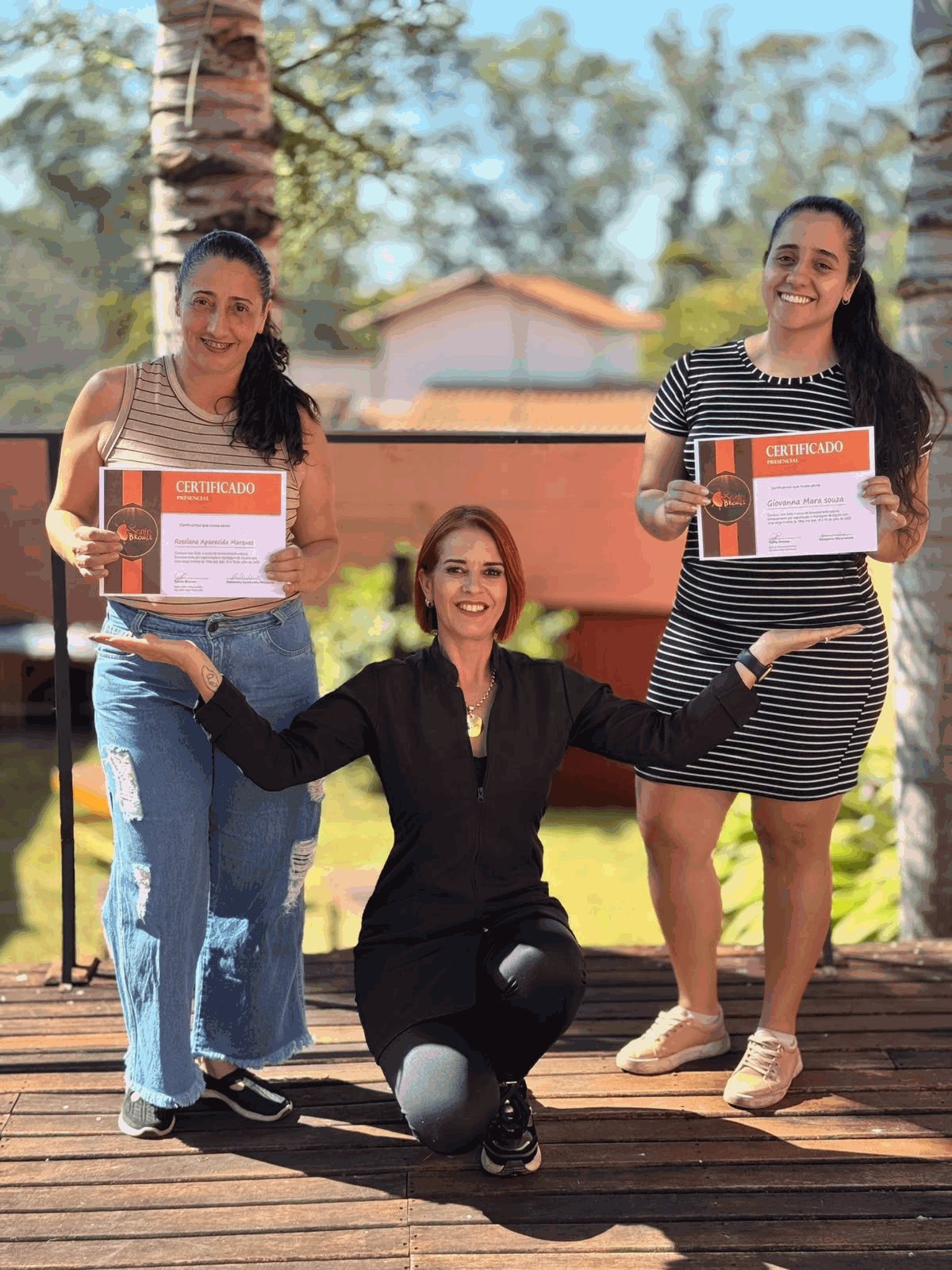Diana Alice ao lado de duas alunas formadas, cada uma segurando o certificado presencial do Santo Bronze.